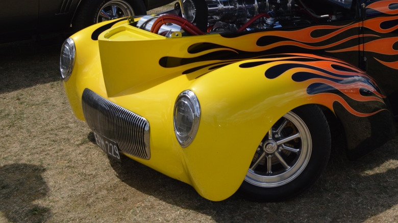 Close-up of the frenched headlights of a hot rod with flame paint, on display with its hood open, showing off its engine.