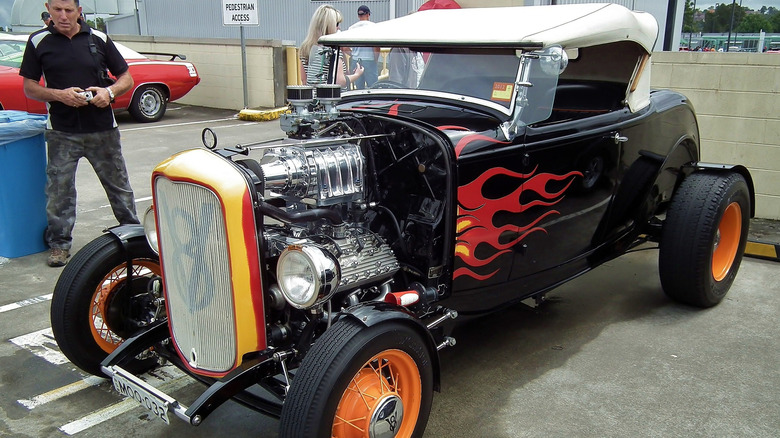 Highboy hot rod sitting in a parking lot, flames painted on its side.