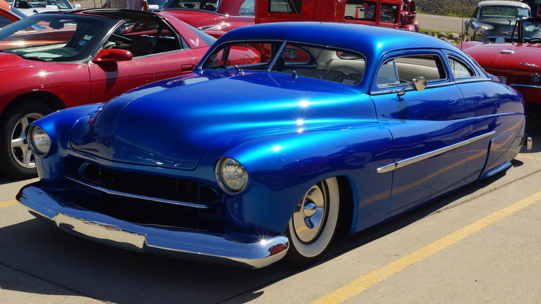 Lead Sled modified 1950 Mercury in a striking blue paint job in a parking lot with other cars in the background.