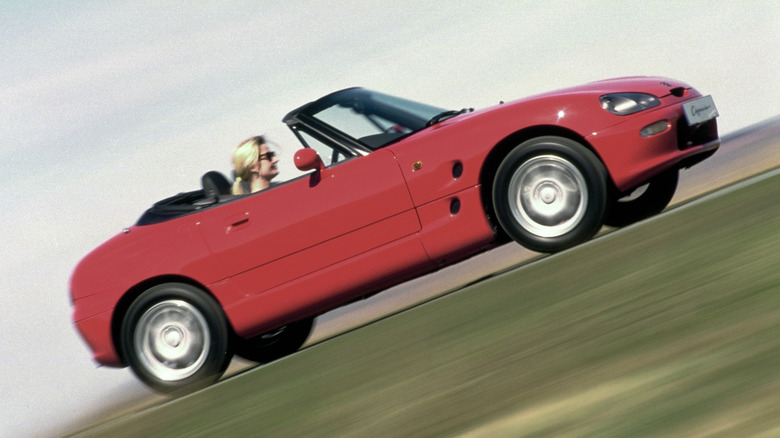 A red Suzuki Cappuccino speeding with a woman inside it