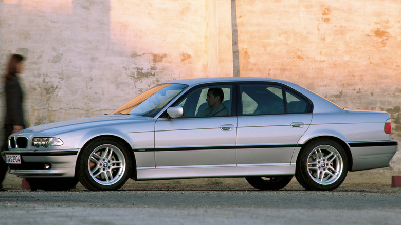 A gray BMW 740d sits parked near an old wall.