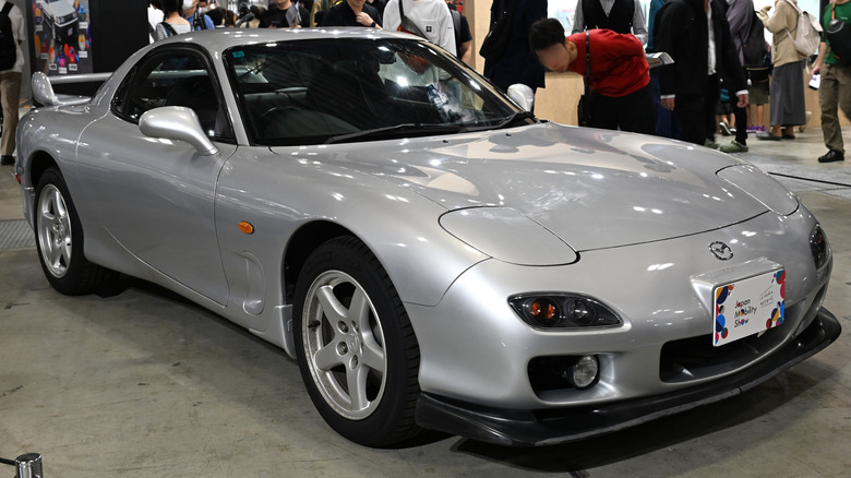 A silver 1999 Mazda RX-7 in a room with people in the background.