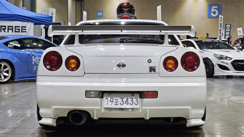 A white Nissan Skyline R34 GT-R, shown from behind in a room with other cars.