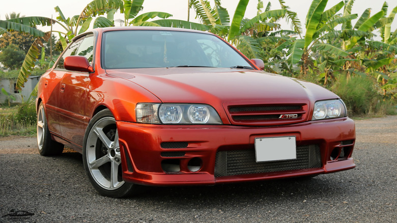 A red Toyota Chaser with greenery behind.