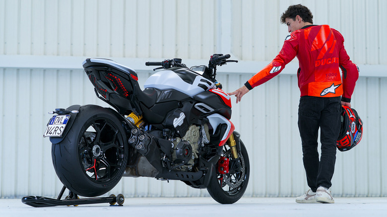 A 2026 Ducati Diavel V4 RS parked on a stand in front of a fence with a rider touching it.