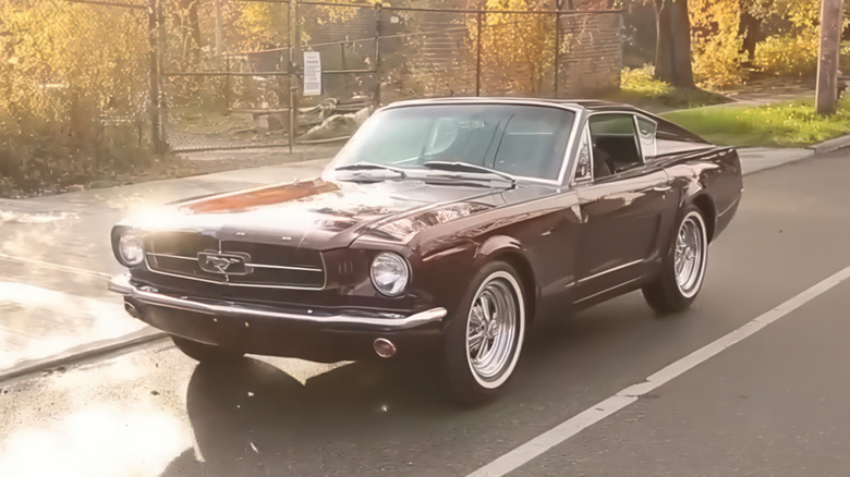 A deep metallic burgundy custom two-seat Ford Mustang "Shorty" fastback driving down a sunlit city street.
