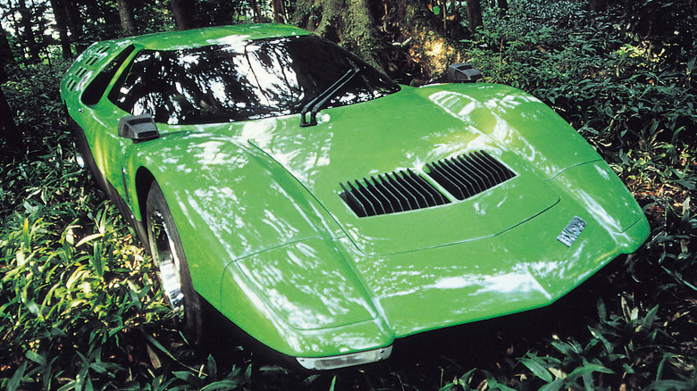 The low-slung, bright green 1970 Mazda RX-500 rotary concept car parked among dense green foliage in a forest.