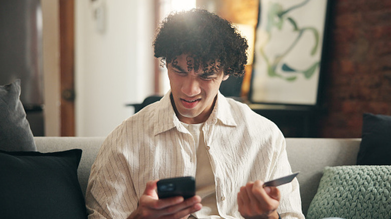 A man is frustrated with phone and credit card in hand.