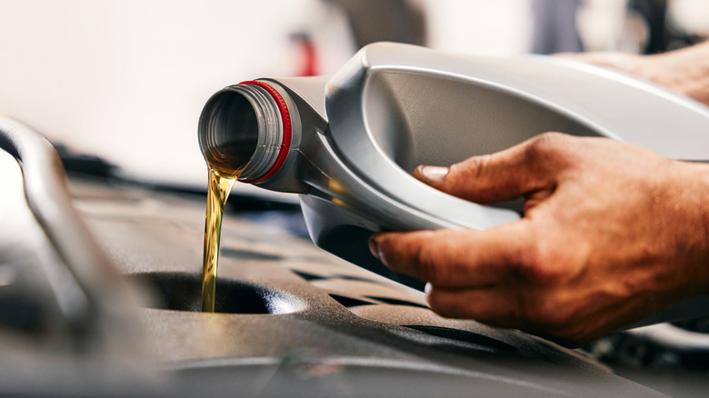 Dirty hands carefully pour oil into a car's engine.