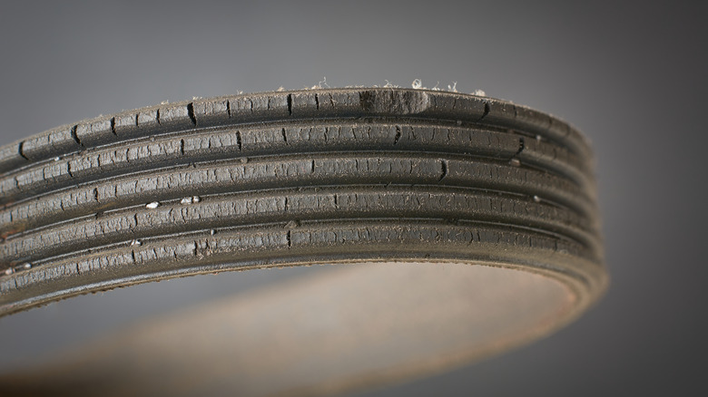 A worn automotive belt is shown close up with deterioration visible.