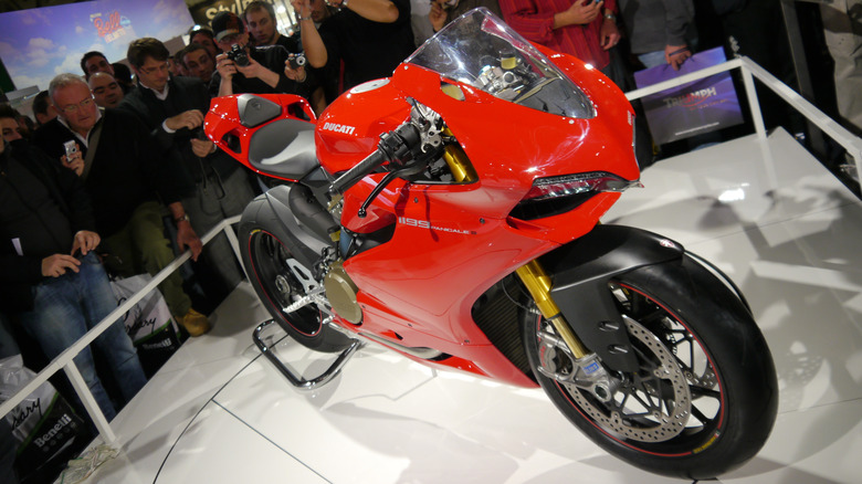 A red Ducati 1199 Panigale sits on a raised platform at an event as people look on and take photos.