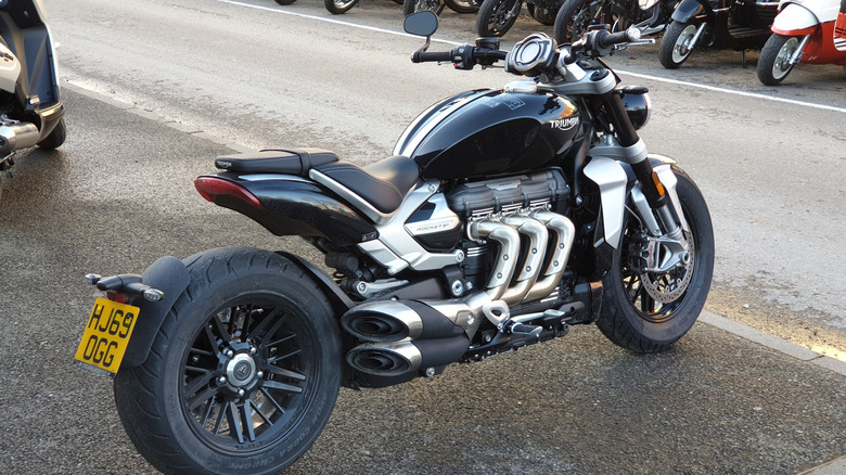 A black and chrome Triumph Rocket shown from the rear against a backdrop of other parked bikes.