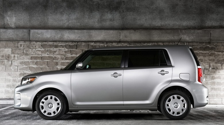 A Scion xB is parked against a brick wall.