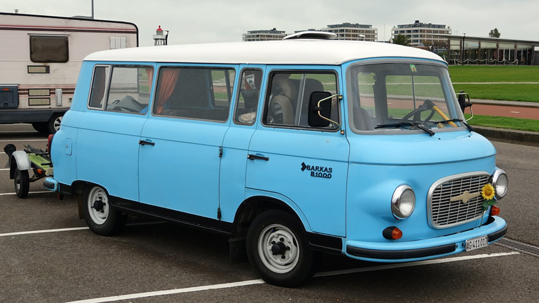 A light blue vintage Barkas B 1000 passenger van with a contrasting white roof, parked in an asphalt lot.