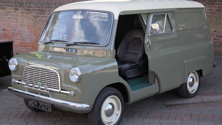 A classic olive-green Bedford CA panel van with a white roof, parked on a brick walkway.