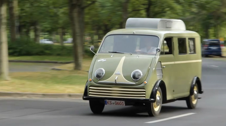 An olive-green vintage DKW Schnellaster van driving along a curved public road.