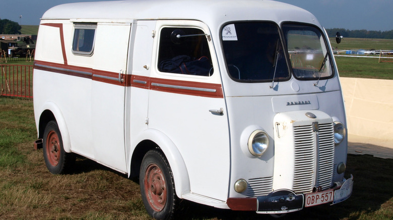 A vintage white Peugeot D3/D4 panel van parked on a grassy field during an outdoor vehicle show.