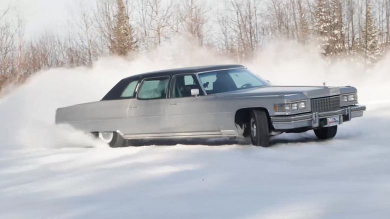 A screenshot showing the silver Caddy fully sideways in a drift in a snowy lot in front of trees