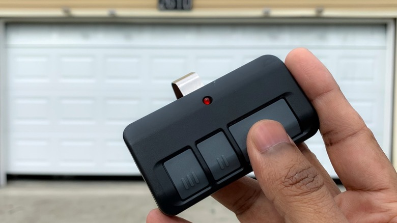 Hand holding a three-button remote in front of a white garage door