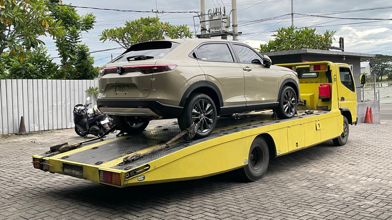 An olive colored SUV being towed on a yellow flatbed truck