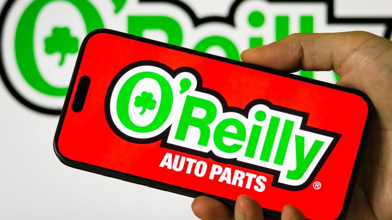 a hand holds a cell phone that displays the O'Reilly Auto Parts logo