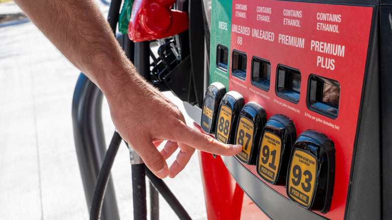 Man's finger points to Unleaded 87 octane fuel pump at a gas station.
