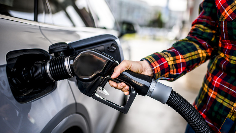 An individual in a flannel holds a gas pump to their car to fill it up.