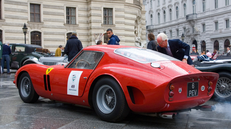 A beautiful red Ferrari GTO on display in a public square amongst other collector car fare.