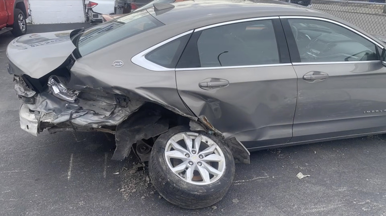 Side view of a gray Chevy Impala with the right rear corner smashed in and the wheel hanging off the car