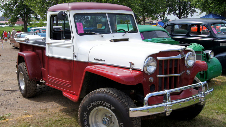 Red and white 1958 Willys Jeep pickup truck right front quarter view parked at an outdoor car show