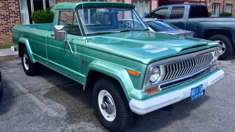 Green 1974 Jeep J-10 pickup right front quarter view parked in front of an apartment building