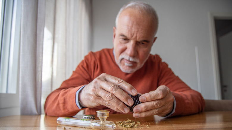 An elderly man grinds marijuana flower for personal use
