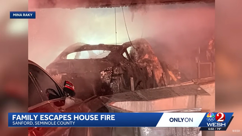a screenshot of the news broadcast showing the charred remains of a Tesla Model Y inside a smoky structure