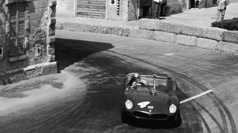 A period photo of a car taking a sharp turn through town.