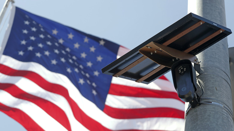 An American flag flying behind a Flock camera