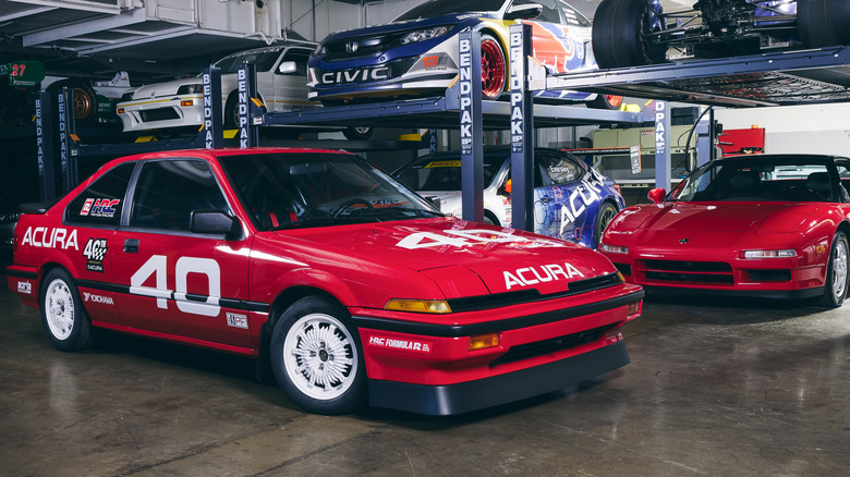 A front three-quarters of the Integra 40 Racer parked in a garage in front of bendpak lifts with other Honda race cars and a shiny red NSX