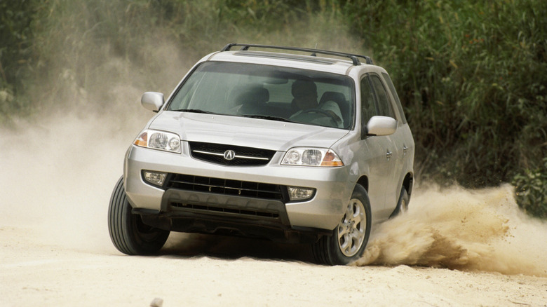 Head-on shot of a silver 2001 MDX kicking up sand off-road in front of green plants