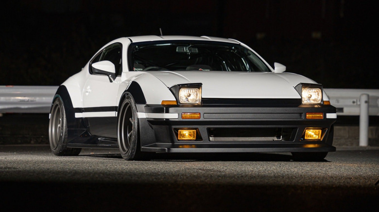 A first-generation Toyota 86 in white with pop-up headlights and a Sprinter Trueno-style front bumper