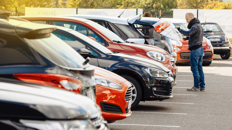 A person examines a trunk hatch in a dealership parking lot.