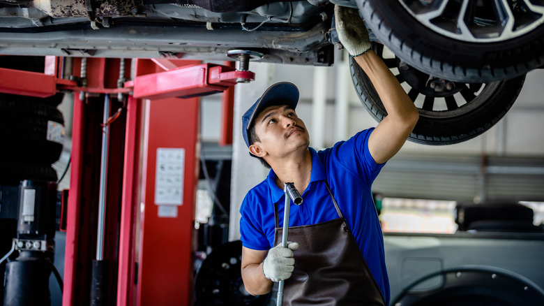 A mechanic inspects a vehicle from below.