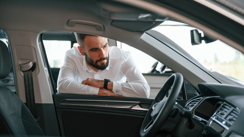 A person with a white shirt eyes an odometer with suspicion through a car's window.