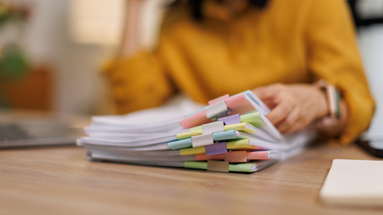A person sitting at a desk flips through stacks of papers.