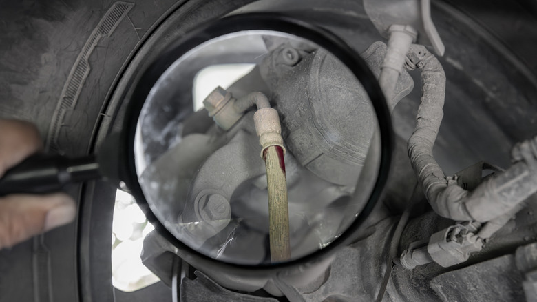 A close-up shot of a person inspecting a brake line with a magnifying glass.