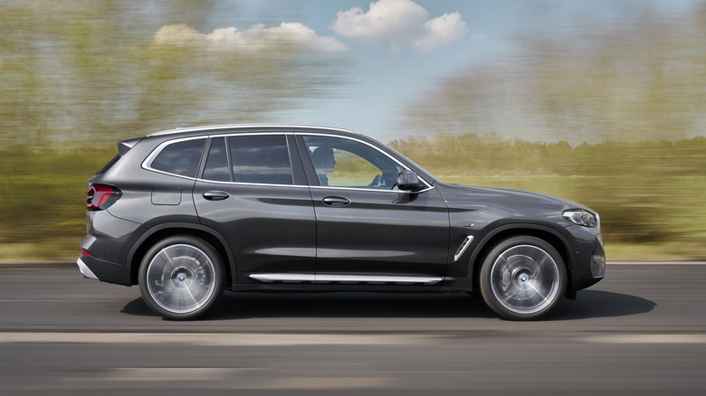 Side view of a black 2021 BMW X3 driving down the road with trees in the background