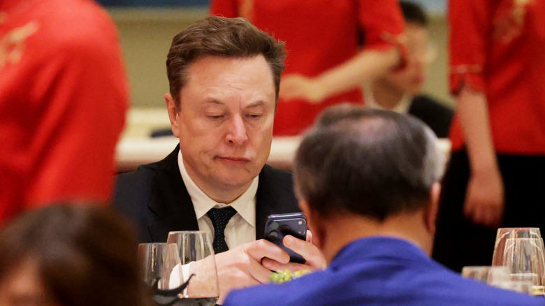 Elon Musk frowns at his phone while on a trip to China with Trump