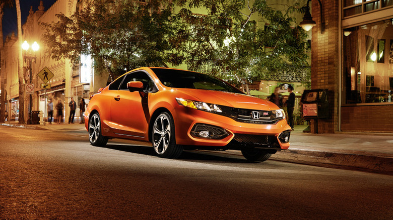 Front 3/4 view of an orange 2015 Honda Civic Si coupe on a city street at night