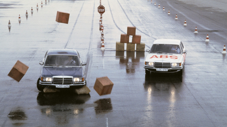 ABS tests on a wet road surface with two identical vehicles of the S-Class series W 116. The left-hand model without ABS slides into the obstacle during emergency braking due to the locking wheels despite fully turned steering. The right vehicle with ABS still remains steerable despite full braking. The driver can brake and steer around the obstacle at the same time.
