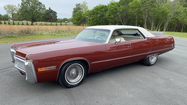 Front three-quarters photo of a burgundy 1973 Chrysler Imperial sedan with a white vinyl roof parked on asphalt in front of grass and trees