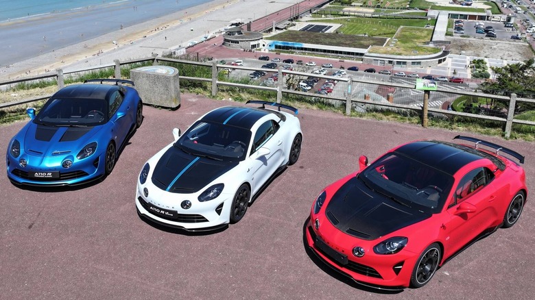 An overhead shot of three A110Rs parked on red concrete in front of a view of a beachside town