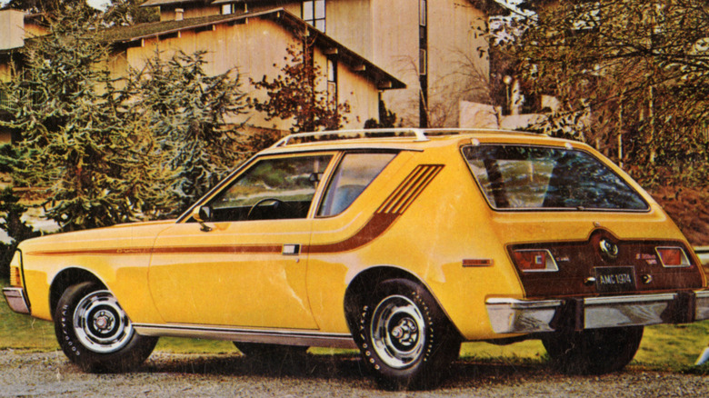 A yellow American Motors Corporation Gremlin X sedan in front of trees and a building in 1974.